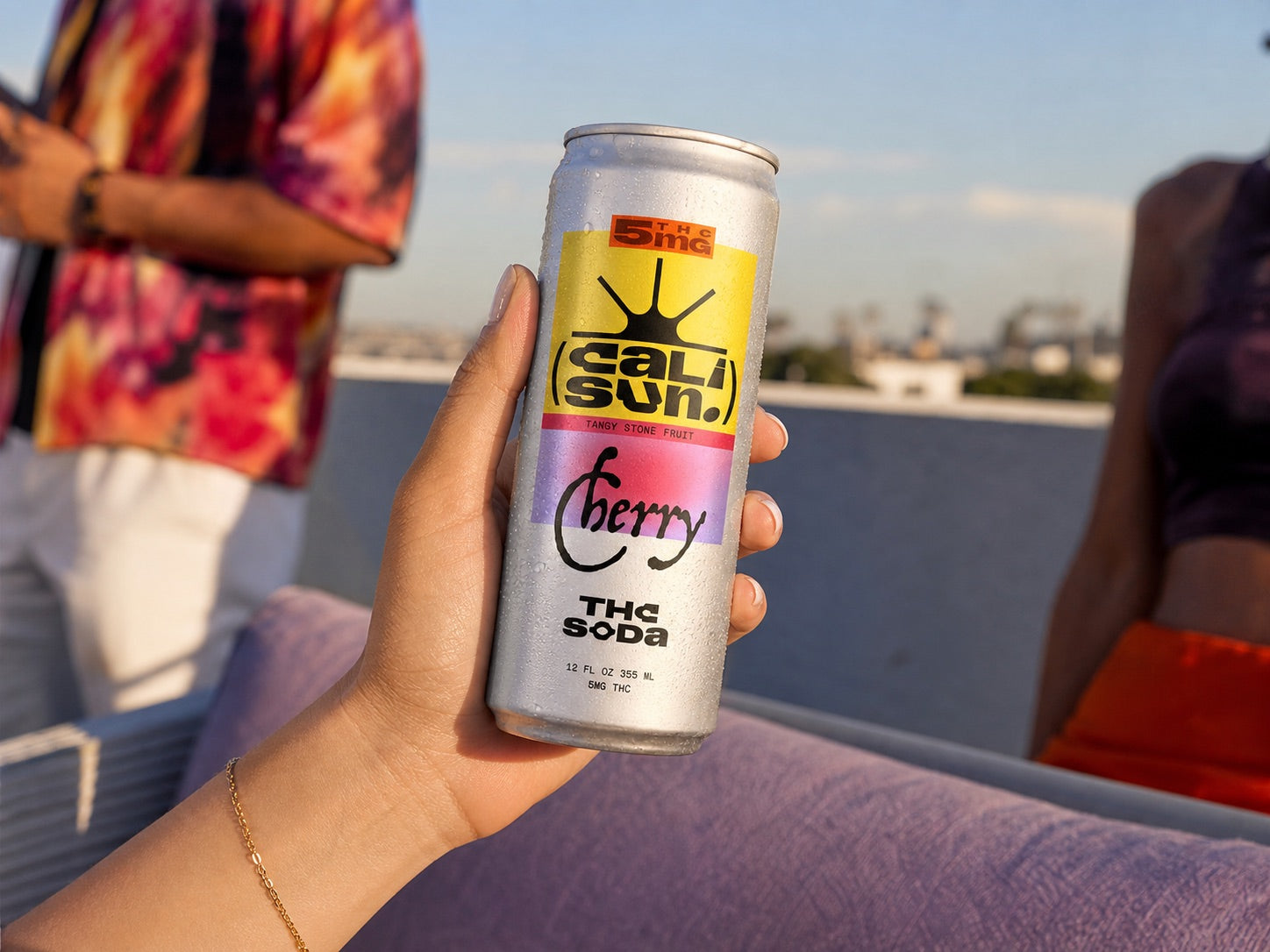 A chilled Cherry Cali Sun can held at a sunny rooftop gathering